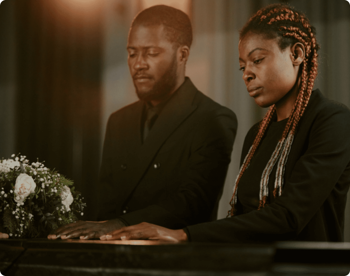 Two people in mourning sitting by a coffin.