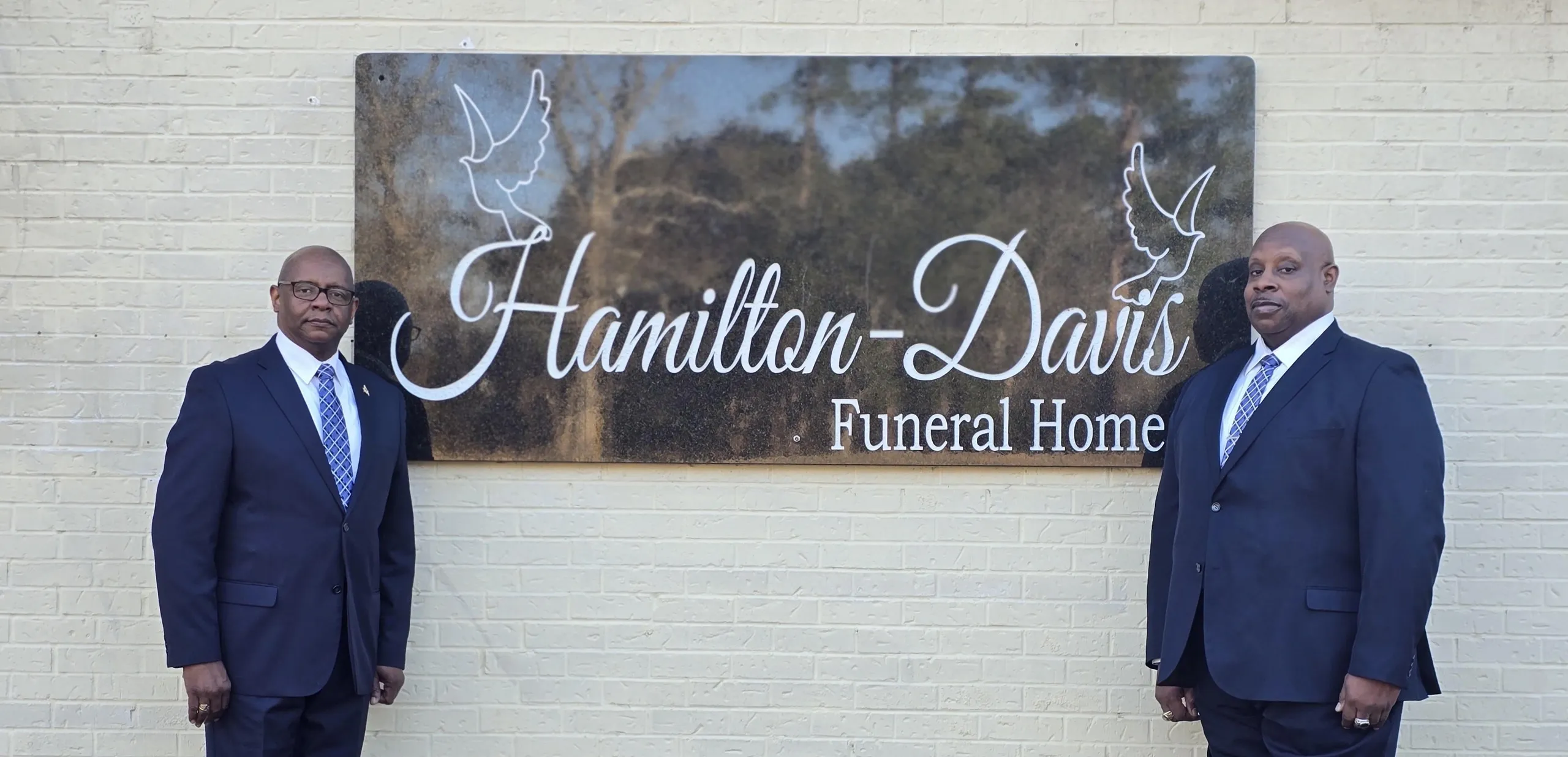 Two men in suits by funeral home sign.