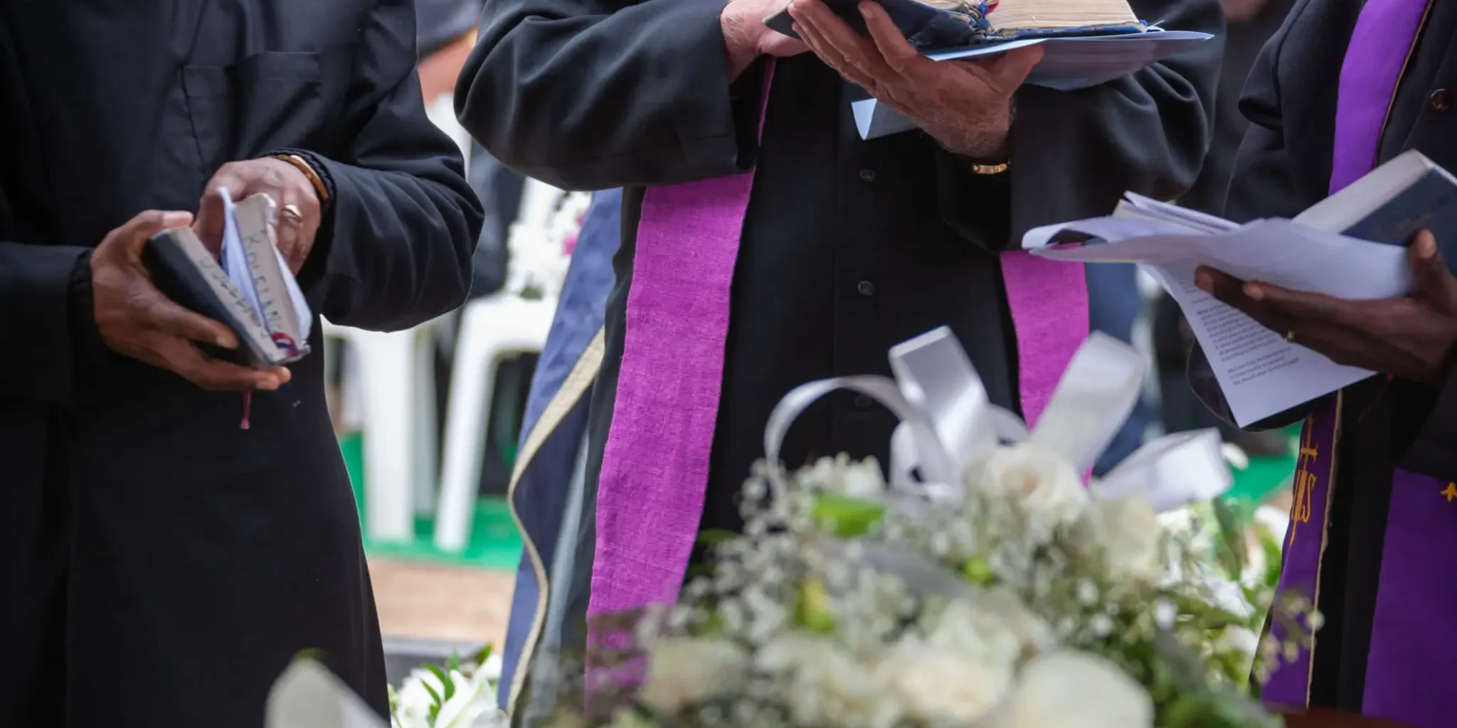 Clergymen holding Bibles during a funeral ceremony.