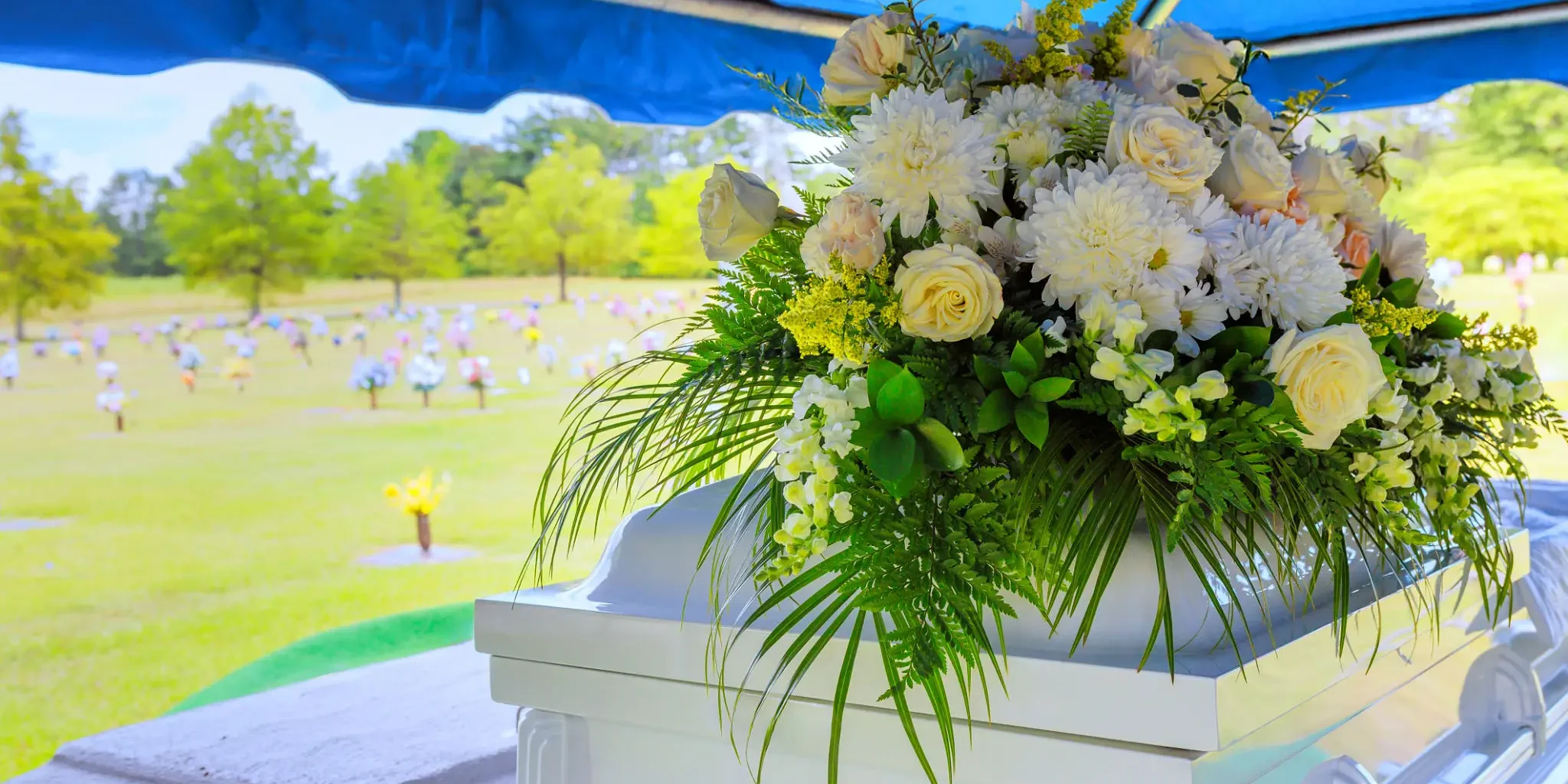 Floral arrangement on a white stand under a blue canopy at an outdoor event.