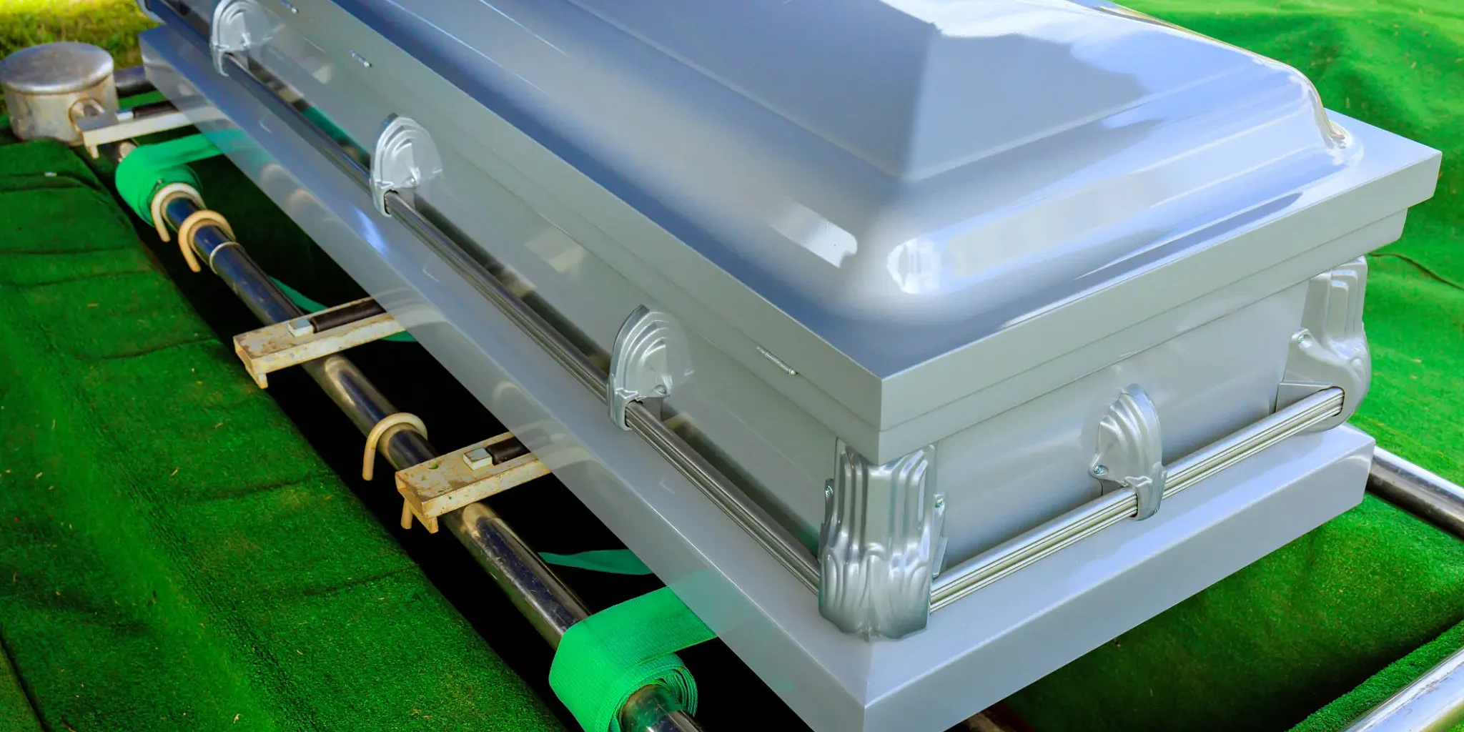 A closed silver coffin on a green surface.